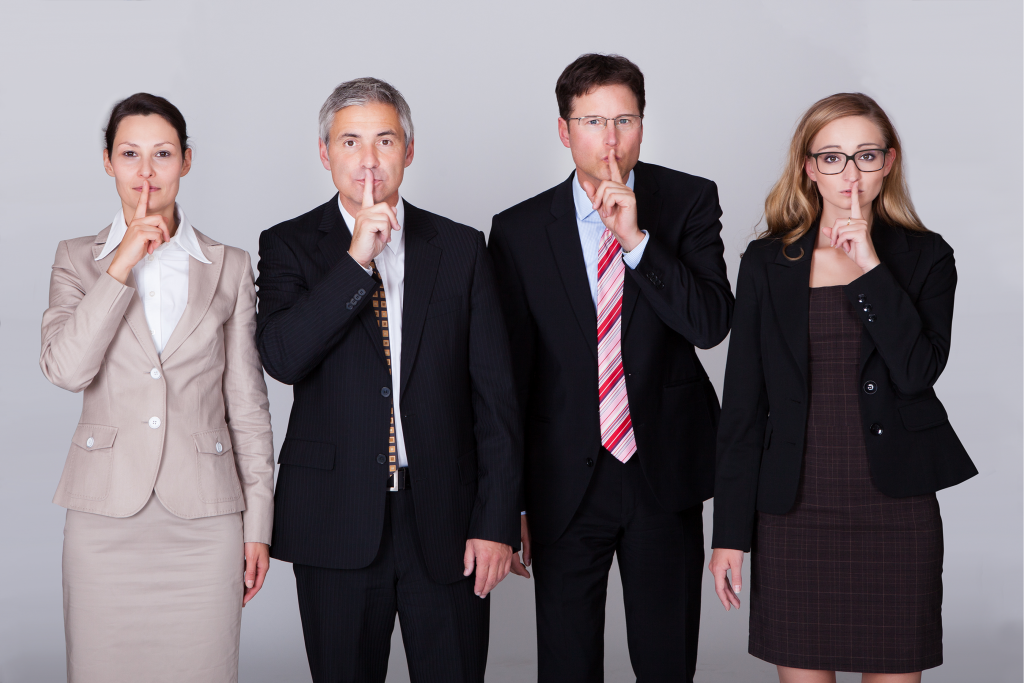 Four diverse businesspeople standing in a row gesturing for silence
